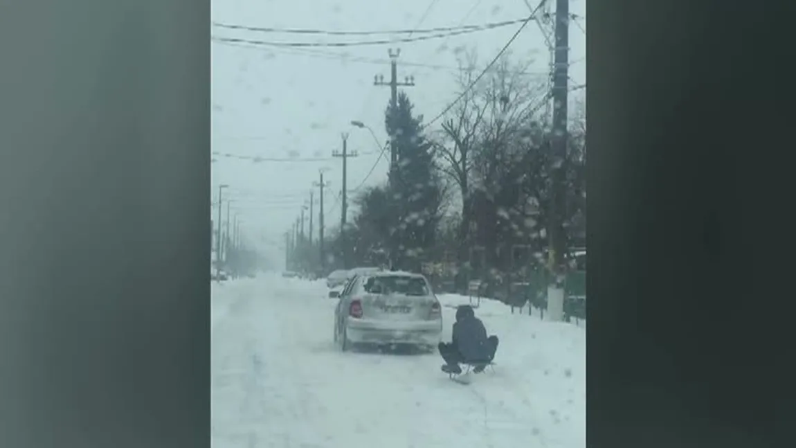 Distracţie periculoasă: Un bărbat s-a dat cu sania trasă de o maşină pe drum