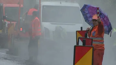 Drumarii din Gorj asfaltează o şosea pe ploaie torenţială